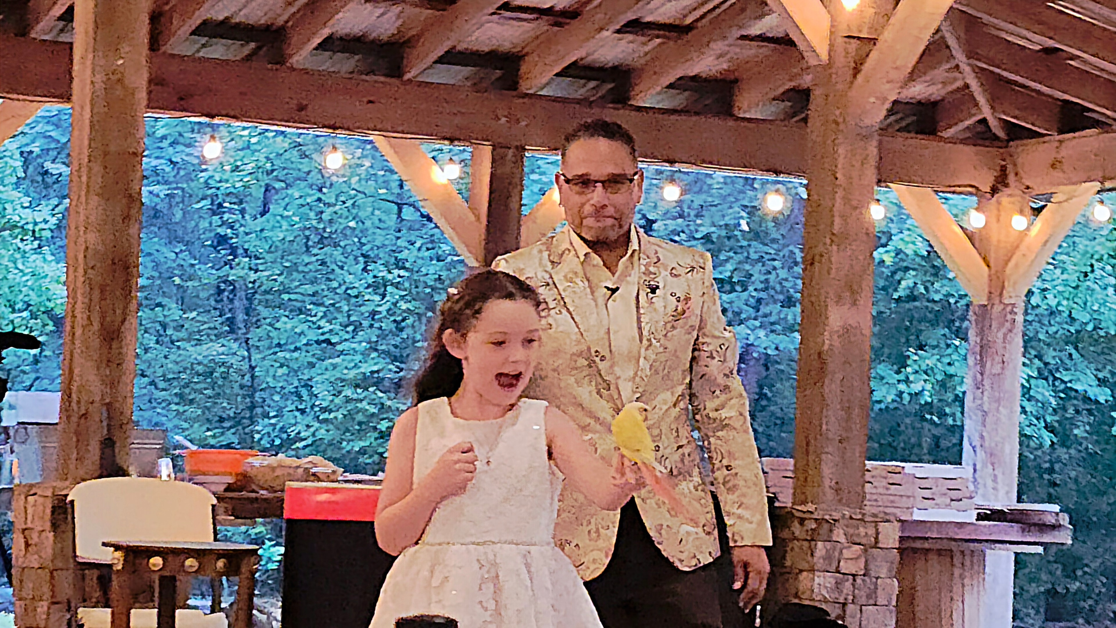 Young girl amazed holding Starbust the Conure with C. Magic at outdoor pavilion wedding